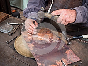 Detail of a craftsman engraves a copper plate with a hammer and chisel
