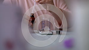 Detail cropped shot of unrecognizable female artisan craftperson dropping essential oil into glass bottle using pipette