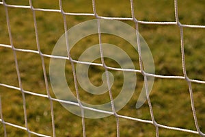 Detail of crossed soccer nets, soccer football in goal net with natural grass on football playground in the background