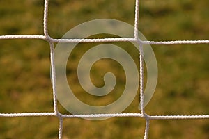 Detail of crossed soccer nets, soccer football in goal net with natural grass on football playground in the background