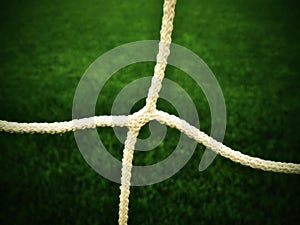 Detail of crossed soccer nets, soccer football in goal net with plastic grass on football playground in the background