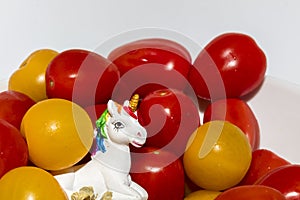 Detail on a cute little unicorn sculpture surrounded by orange and roma tomatoes in a white bowl