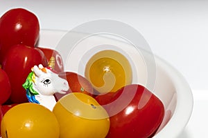 Detail on a cute little unicorn sculpture surrounded by orange and roma tomatoes in a white bowl