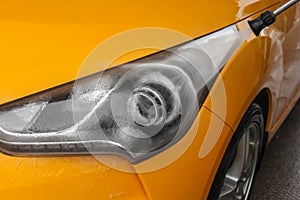 Detail on dark yellow car front light being washed with jet water in carwash.