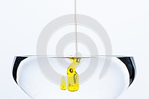 Detail of dash of olive oil drops gliding into glass of water isolated on white background