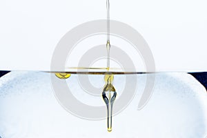 Detail of dash of olive oil drops gliding into glass of water isolated on white background