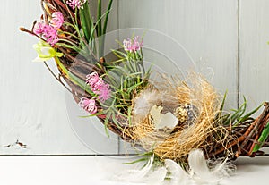 Detail of a decorative spring wreath made of twigs and flowers, with a small bird`s nest. Close-up on a gray wooden background