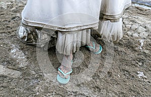 Detail of dirty white wedding dress and filthy foot covered by mud and dirt