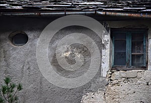 Detail of the facade of an old house, with oval and window with glass made opaque by time, in Vergemoli.
