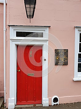 Detail from the facade of a pink cottage with a bright red door in the county of Essex, United Kingdom.