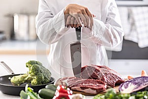 Detail of female chef leaning on knife with its top cut into a chunk of red meat