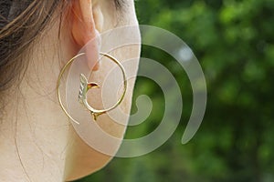 detail of female ear wearing metal decorative shape earring