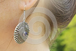 detail of female ear wearing metal decorative shape earring