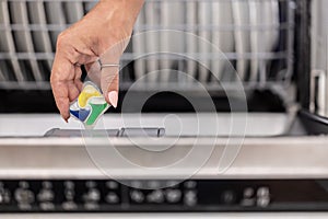 Detail of a female hand putting colorful detergent tablet into the dishwasher