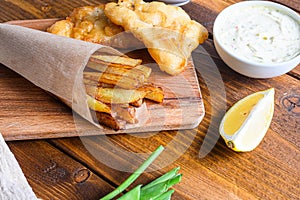 Detail of fish chips with dip and lemon, mashed minty peas, tartar sauce in paper cone  on wood chopping board dip and lemon -