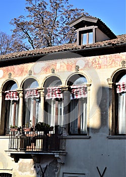 Detail, with French windows and balcony, of a historic house illuminated, in part, by the sun in the blue sky.