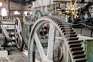 Detail of a gear of a vintage rolling mill. Blurred, old fashioned machines and industrial factory interior in the background