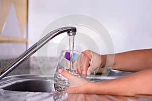 Detail of a girl`s hands, rinsing a freshly washed glass in the kitchen sink. Helping with the housework