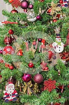 Detail of green Christmas (Chrismas) tree with colored ornaments, globes, stars, Santa Claus, Snowman