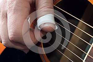 Detail of a guitar player hand using a thumbpick to play fingerstyle and fingerpick music
