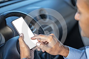 Detail of the hand of a driver holding a mobile phone with a blank screen on the steering wheel of the car with copy space