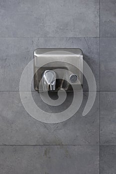 Detail of a hand dryer hanging on a gray tile wall. Front view