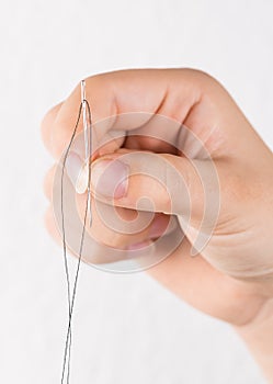 Detail of hand holding needle with thread on white background