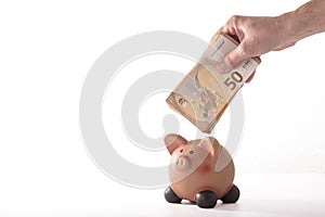 detail of a hand inserting a fifty euro banknote into a piggy bank, concept for business and save money on white