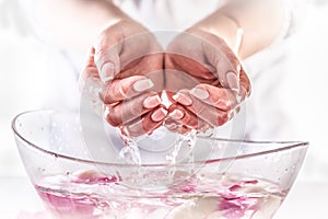 Detail of hand with perfect manicure raised from a glass bowl full of water with flower petals