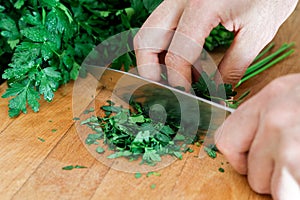 Detail of hands chopping up a bunch of parsley on wood chopping