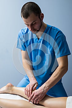 Detail of hands massaging human calf muscle. ManTherapist applying pressure on female leg.