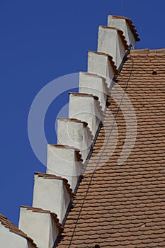 Detail of a historic house roof in front of blue summer sky, roof top to the red tiled roofs of the historic house