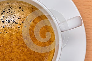 Detail of hot black coffee with foam bubbles in white cup with b