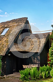 Detail of a house with old thatched roof and a wood seating area