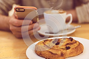 Detail image of unrecognisable man drinking coffee and holding smart phone while having breakfast in restaurant.