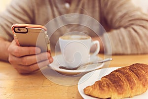Detail image of unrecognisable man drinking coffee and holding smart phone while having breakfast in restaurant. photo