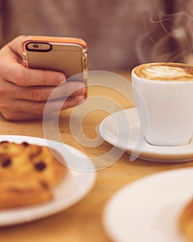 Detail image of unrecognisable man drinking coffee and holding smart phone while having breakfast in restaurant.