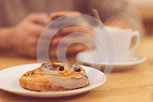 Detail image of unrecognisable man drinking coffee and holding smart phone while having breakfast in restaurant.