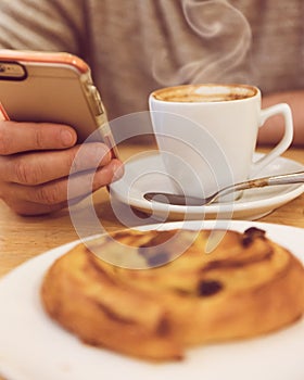 Detail image of unrecognisable man drinking coffee and holding smart phone while having breakfast in restaurant.