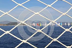 Detail image of wooden pulley with ropes of an classical sailing yacht. ocean and sailing boats in the blurry background