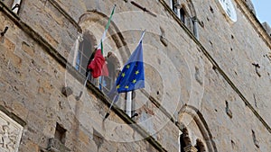 Detail on the Italian and European Union flags hanging on the facade of the ancient Palazzo dei Priori in the historic center of t