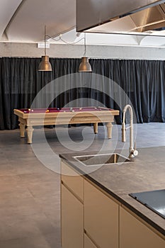 Detail of a kitchen island with a stainless steel sink and a pool table in the background