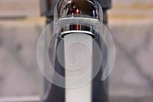 Stream of water falling from a faucet in a sink photo