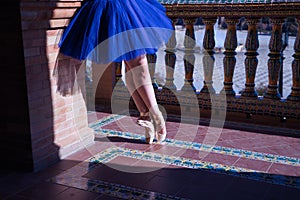 Detail of legs and feet of adult female classical ballet dancer in blue tutu doing figures on the terrace of a square next to a