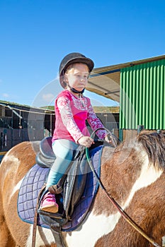 Detail of cute little girl riding a horse next to the stable