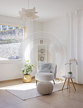 Detail of a living room corner with a small armchair with a coffee table and a pouf resting on the carpet