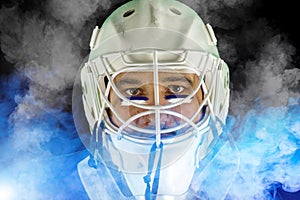 Detail of a male face in a white goalie hockey mask and  blue and white smoke.