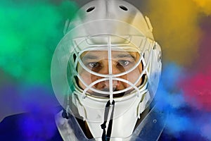 Detail of a male face in a white goalie hockey mask and  colored smoke.