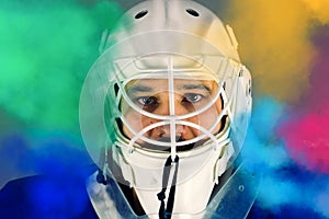 Detail of a male face in a white goalie hockey mask and  colored smoke.