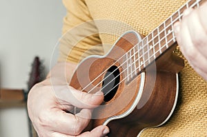 Detail of man with yellow sweater playing a ukulele